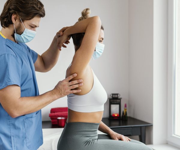 side-male-osteopathic-therapist-with-medical-mask-checking-female-patient-s-shoulder-joint